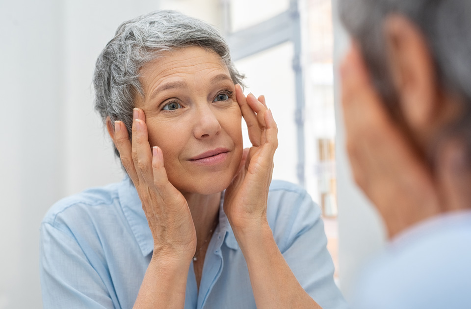 Beautiful senior woman checking her face skin and looking for blemishes