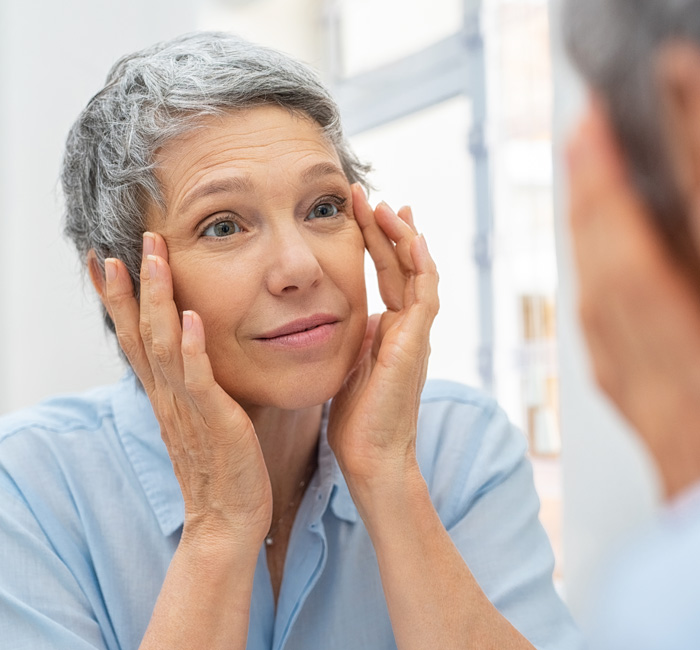 Beautiful senior woman checking her face skin and looking for blemishes